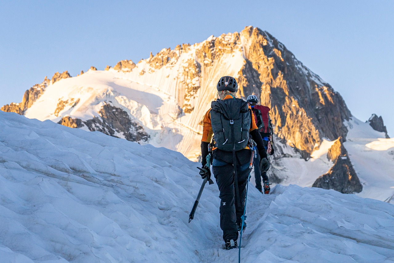 A female climber walking a snowy alpine ridge at sunrise